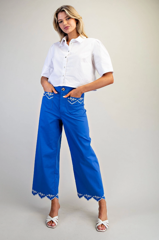 Woman wearing a white shirt and blue pants with lace details on a plain background