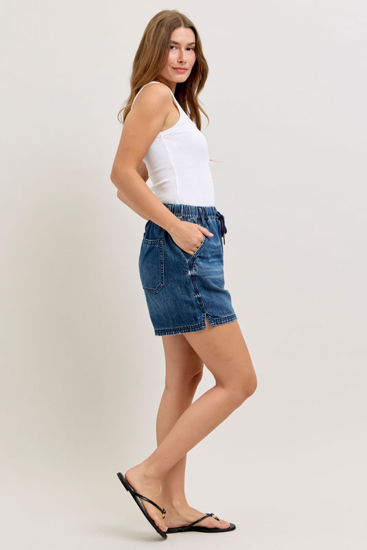 Woman wearing a white tank top and blue denim shorts on a plain background