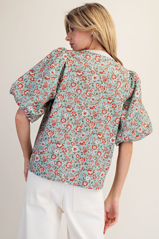 Woman wearing a floral blouse with puff sleeves on a plain background