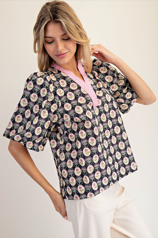 Woman wearing a floral patterned blouse with a pink collar against a white background