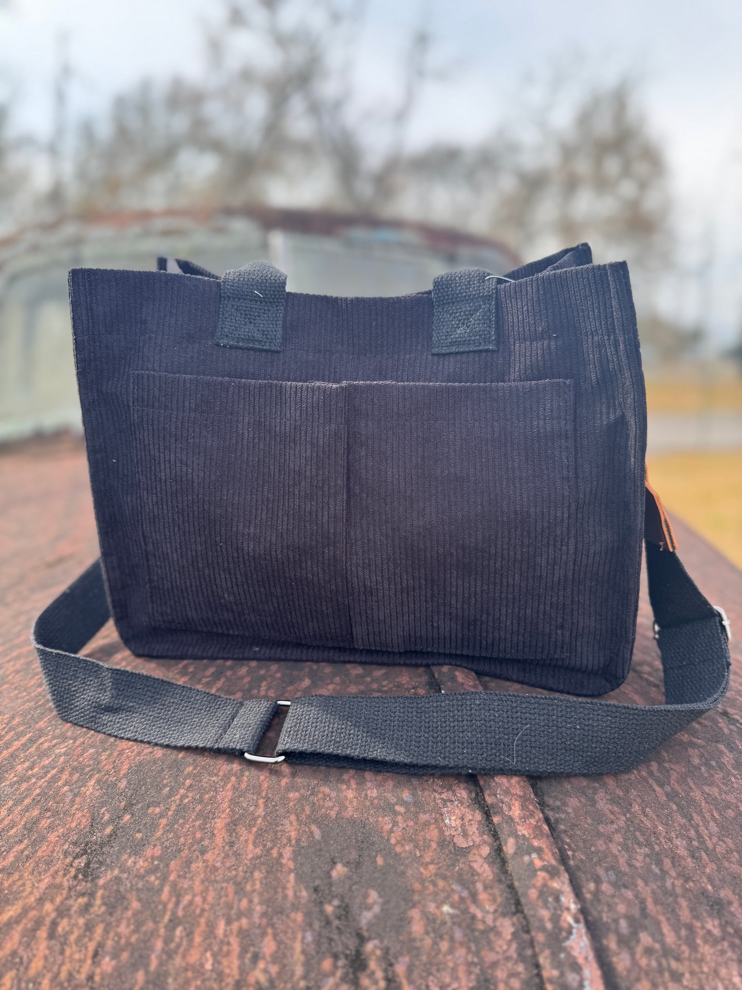 Black tote bag with a strap on a wooden surface
