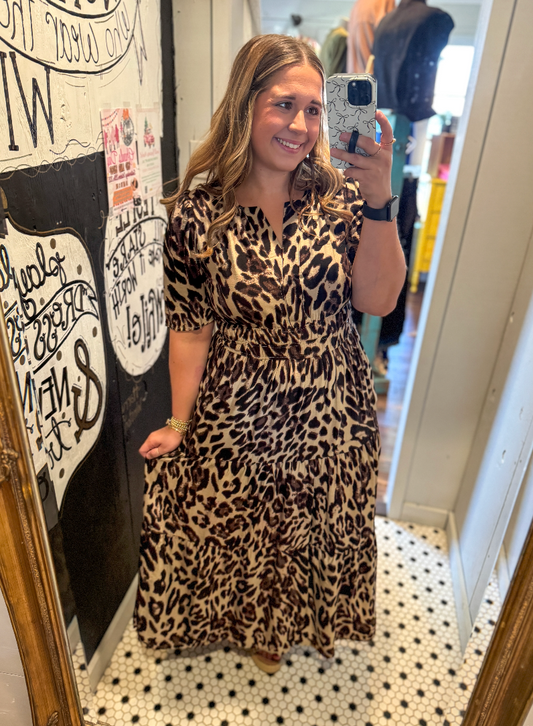 Woman taking a mirror selfie wearing a leopard print dress in a store.