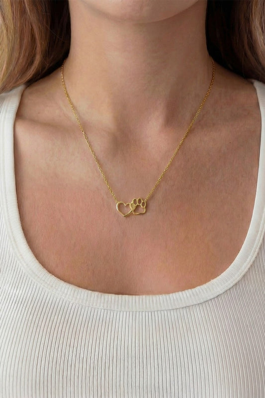 Gold necklace with a heart and paw design worn by a person