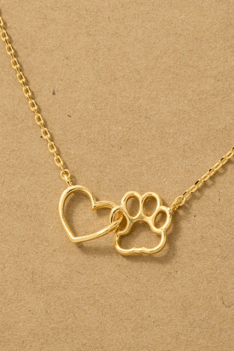 Gold necklace with heart and paw print pendant on a beige background