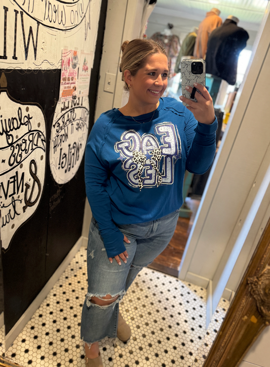 Person taking a mirror selfie wearing a blue sweatshirt with a graphic design and ripped jeans.