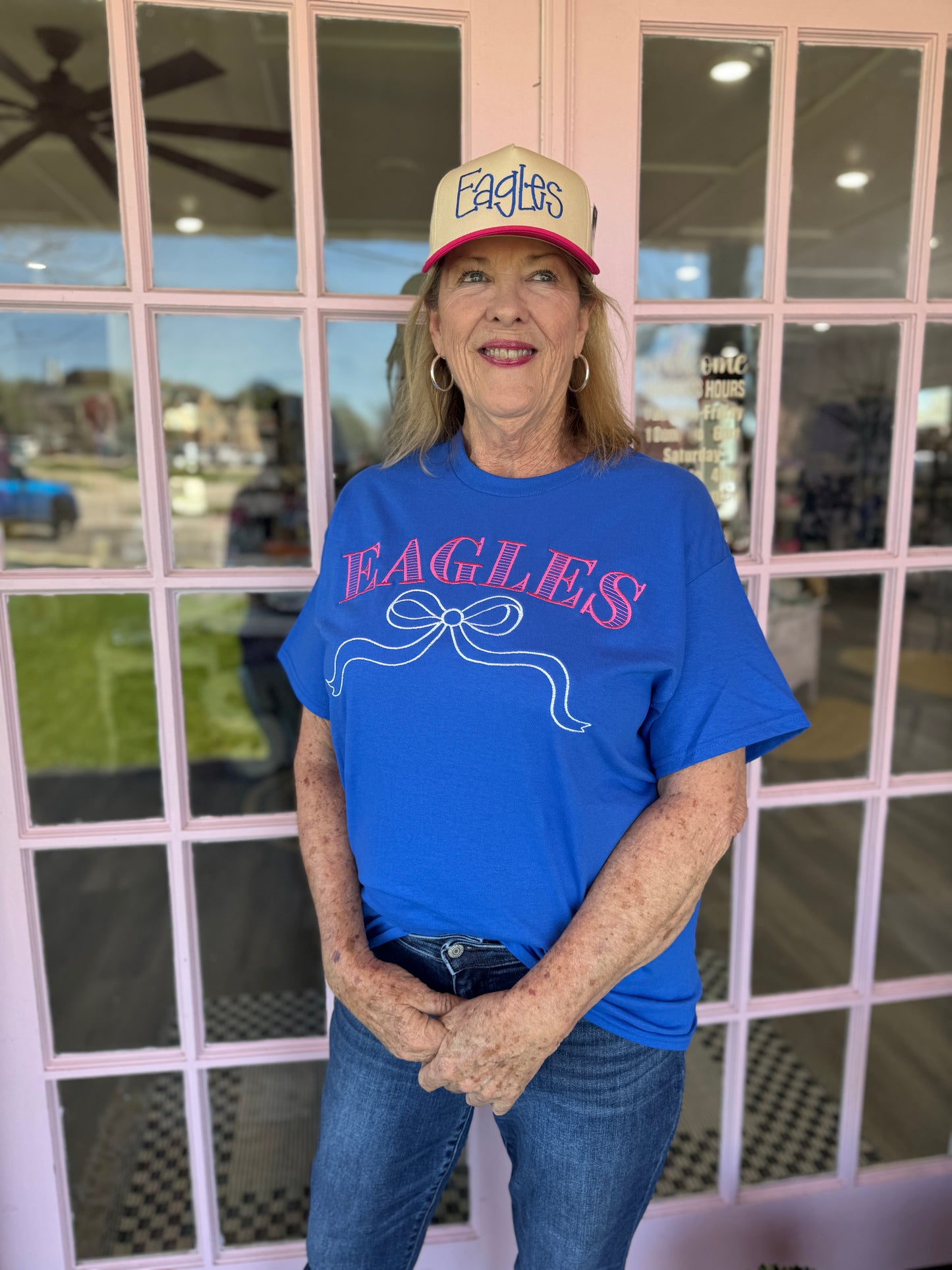 Person wearing a blue 'Eagles' shirt and cap standing in front of a window.