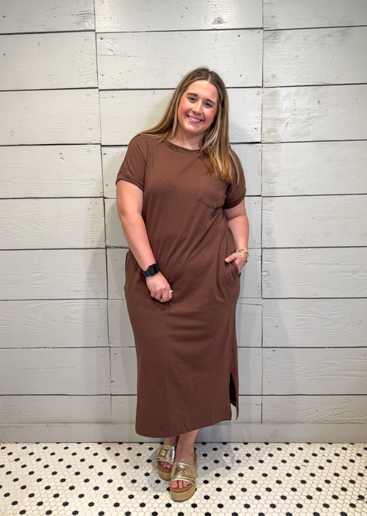 Woman wearing a brown dress standing against a tiled wall.