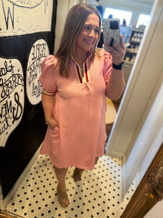 Woman taking a mirror selfie wearing a pink dress in a store.