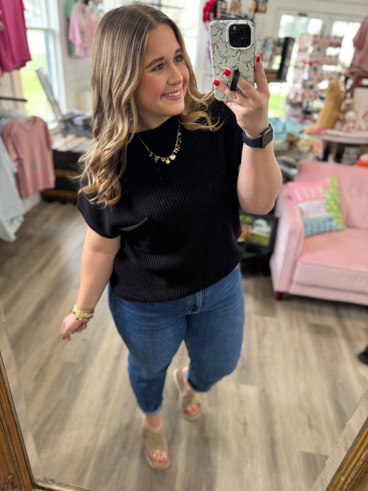 Woman taking a mirror selfie wearing a black sweater and blue jeans in a store.