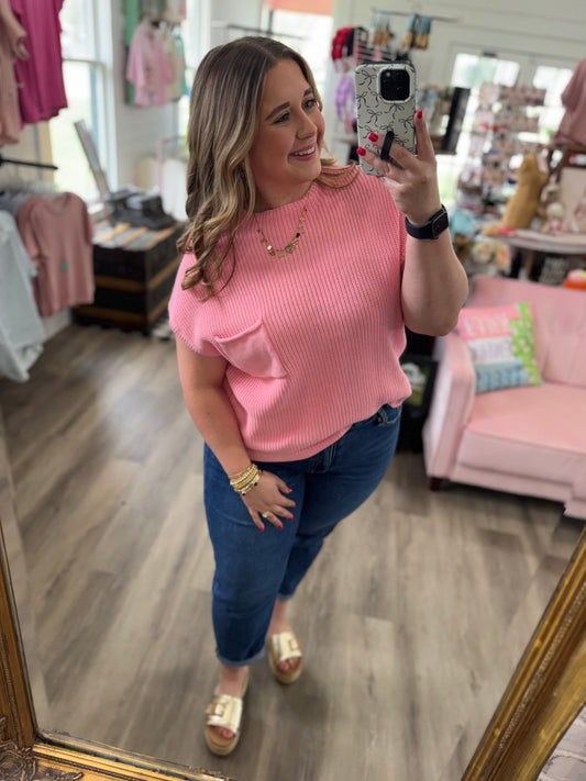 Woman taking a mirror selfie wearing a pink top and blue jeans in a store.