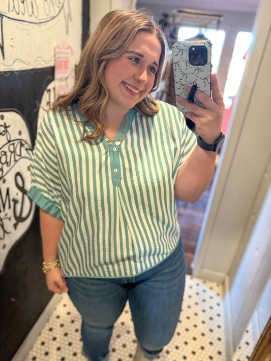 Woman taking a mirror selfie wearing a green and white striped shirt and blue jeans.
