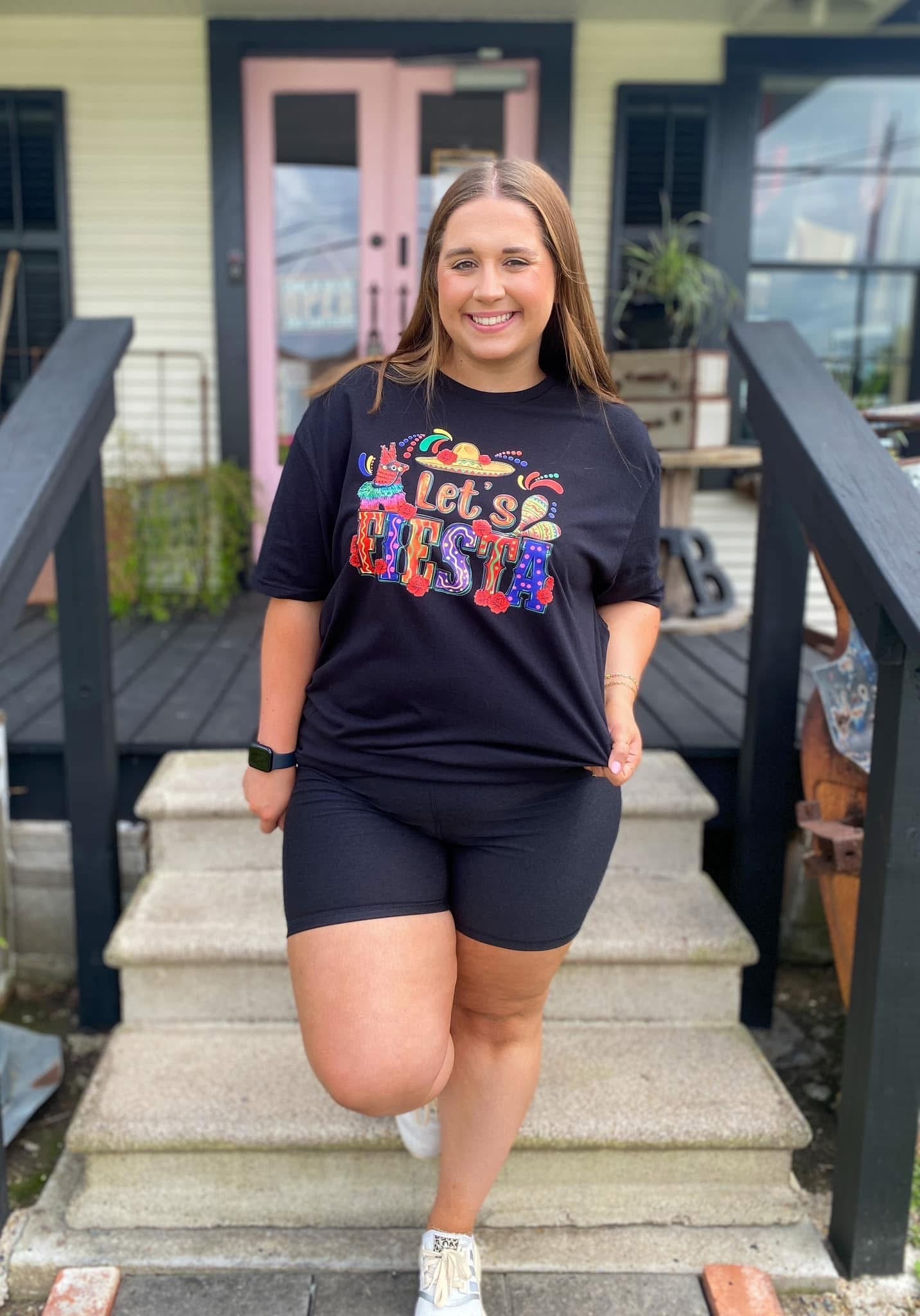Woman wearing a black t-shirt with colorful text and black shorts standing on steps.