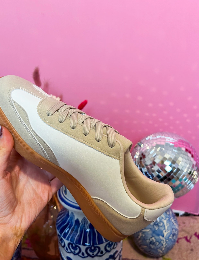 Beige sneaker held by a hand with a pink background and decorative elements.