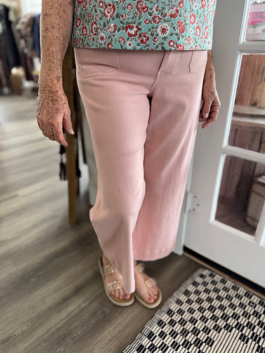 Person wearing a floral top and pink pants in a room with wooden flooring.