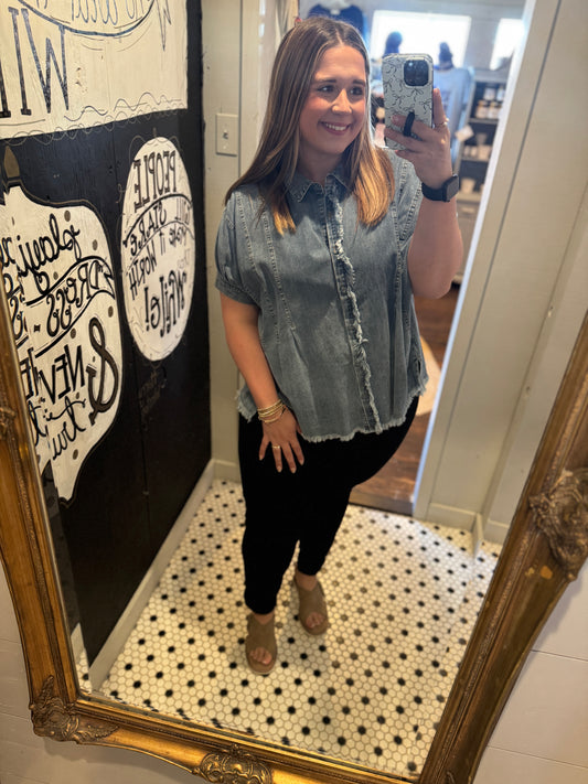 Woman taking a mirror selfie wearing a denim shirt and black pants in a store.