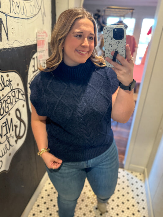 Woman taking a mirror selfie wearing a navy blue cable knit sweater and jeans.
