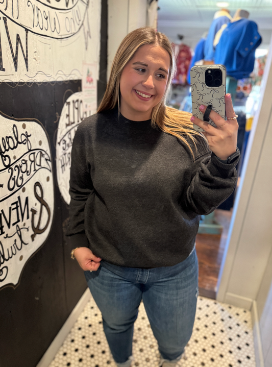 Woman taking a mirror selfie wearing a dark sweater and jeans in a store.
