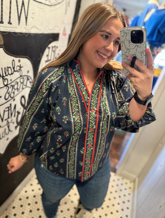 Woman taking a mirror selfie wearing a patterned shirt in an indoor setting.