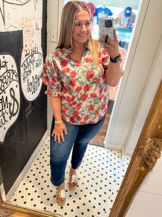 Woman taking a mirror selfie wearing a floral blouse and jeans in a store.