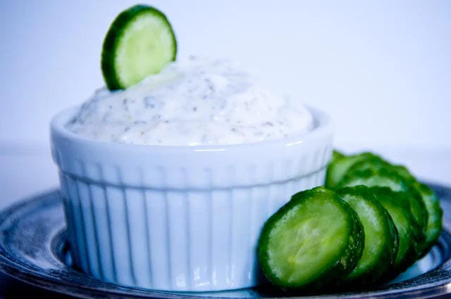 Cucumber slices and a bowl of creamy dip on a white plate