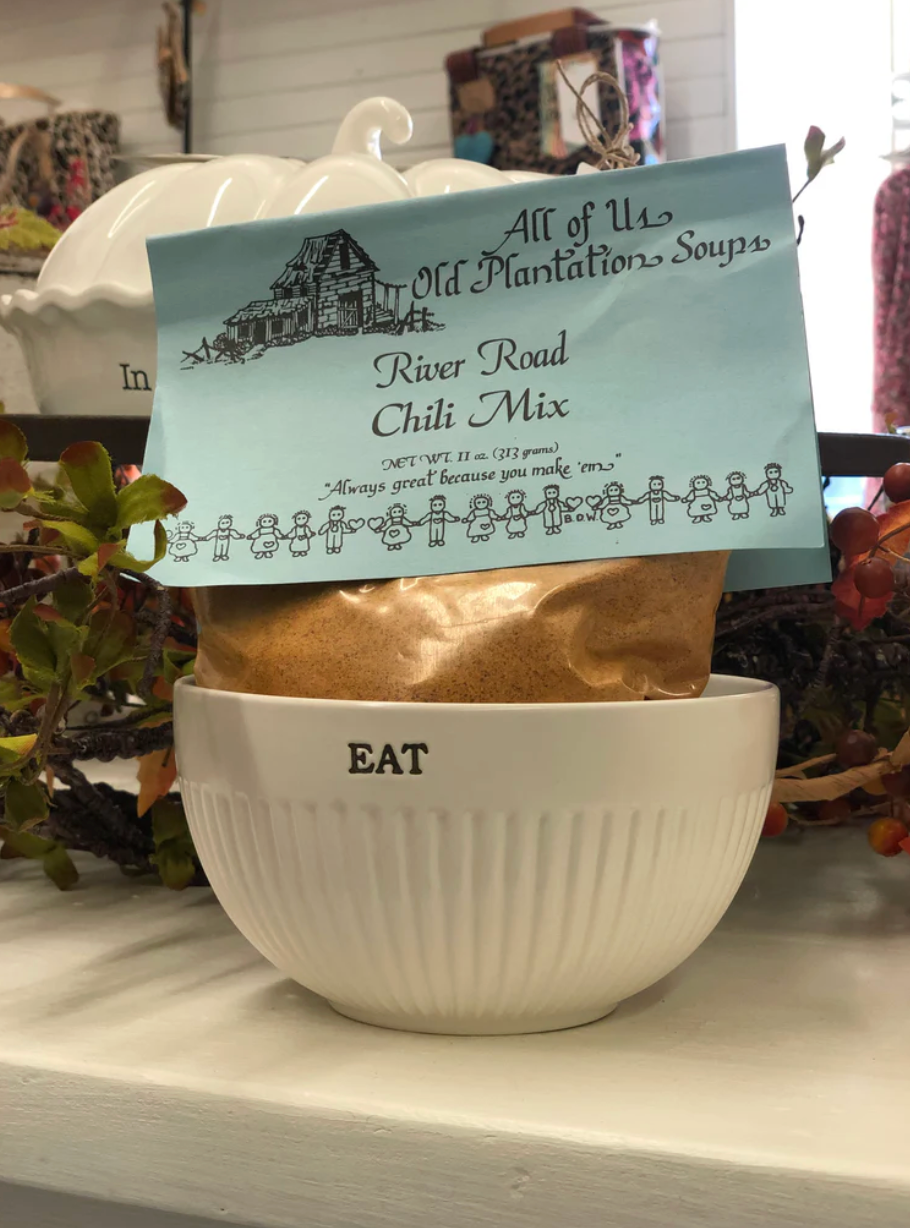 Bag of River Road Chili Mix from All of Us Old Plantation Soups with a white bowl labeled 'EAT' on a decorative surface.