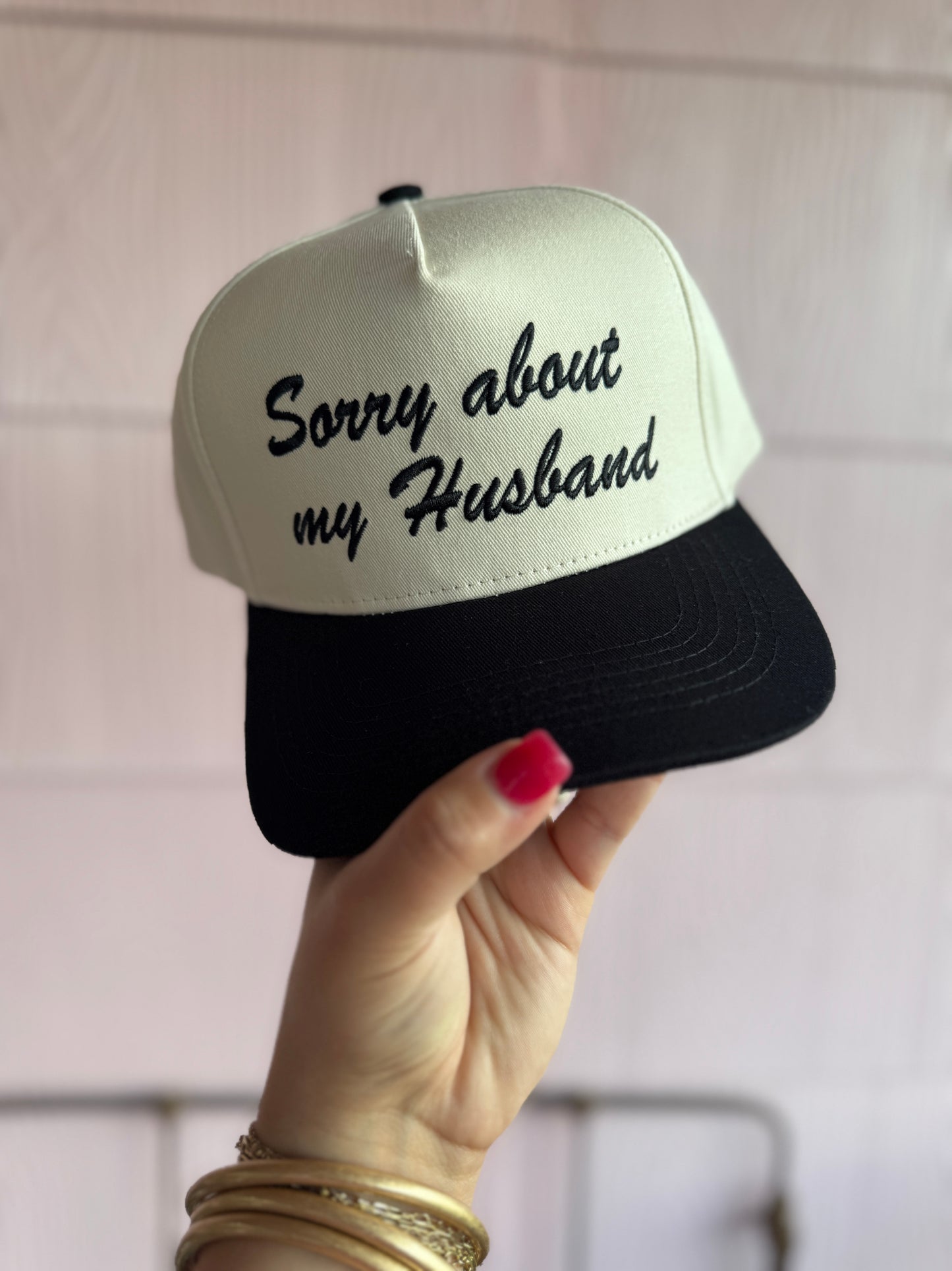 Cap with 'Sorry about my Husband' text held by a hand against a light background