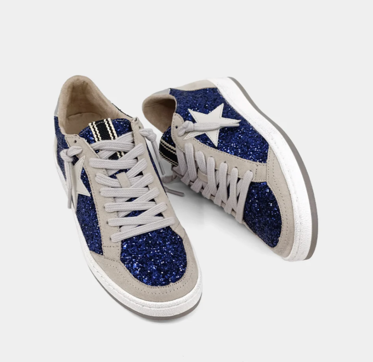 Pair of sneakers with blue glittery soles and white laces on a light gray background