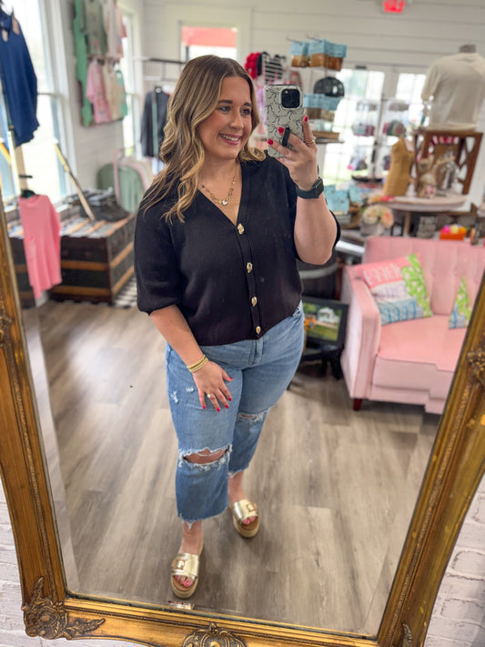 Woman taking a mirror selfie wearing a black cardigan and blue jeans in a store.