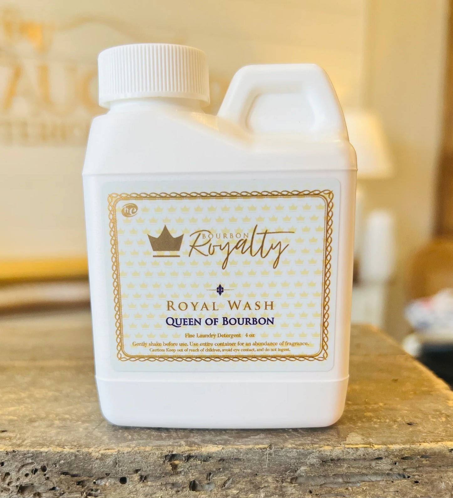White bottle of 'Queen of Bourbon' Royal Wash on a wooden surface with a blurred background.