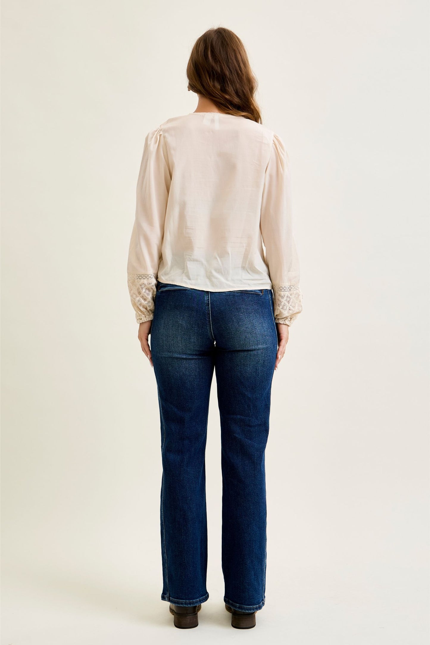Person wearing a beige blouse and blue jeans on a white background