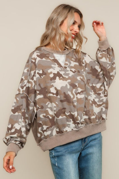 Woman wearing a camouflage sweater and blue jeans against a plain background