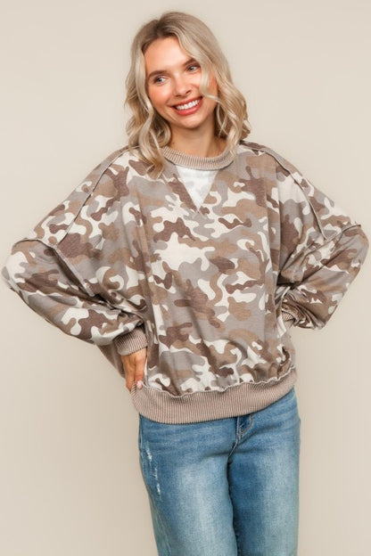 Woman wearing a camouflage sweater and blue jeans against a beige background
