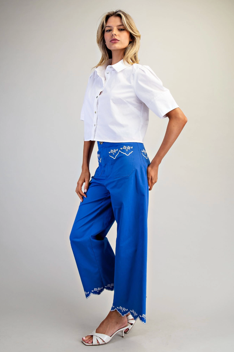 Woman wearing a white shirt and blue pants with lace details on a plain background