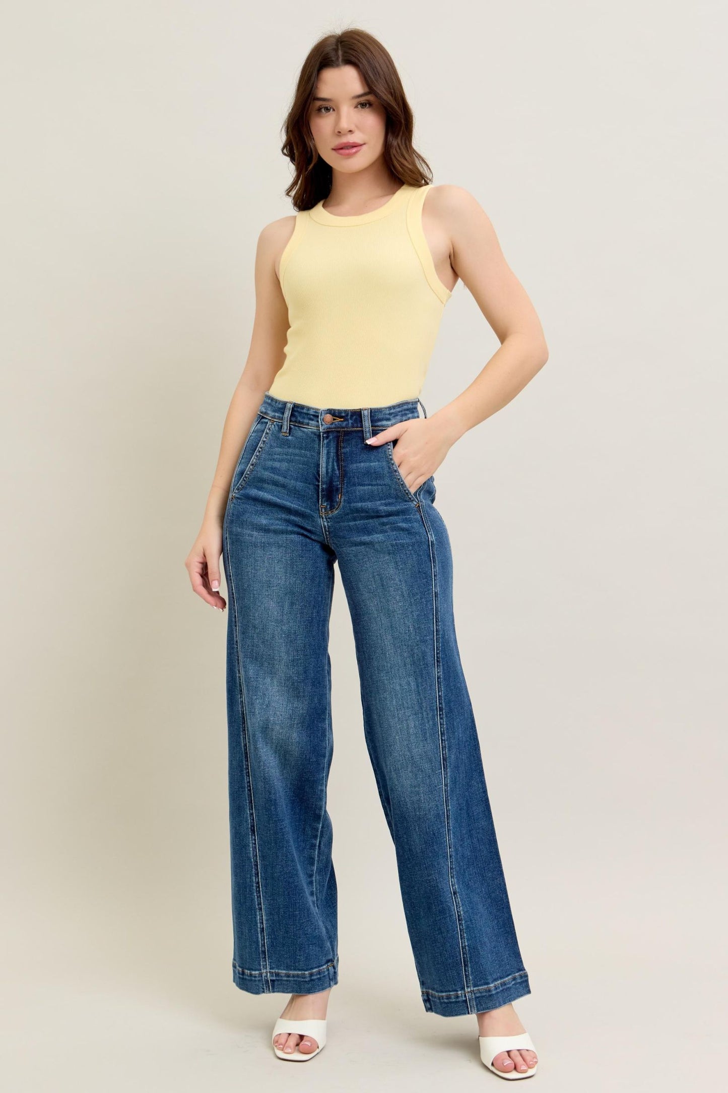 Woman wearing a yellow sleeveless top and blue jeans on a plain background