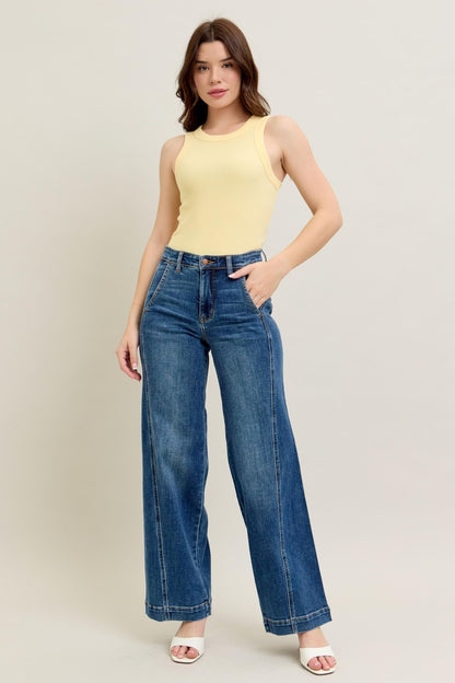 Woman wearing a yellow sleeveless top and blue jeans on a plain background