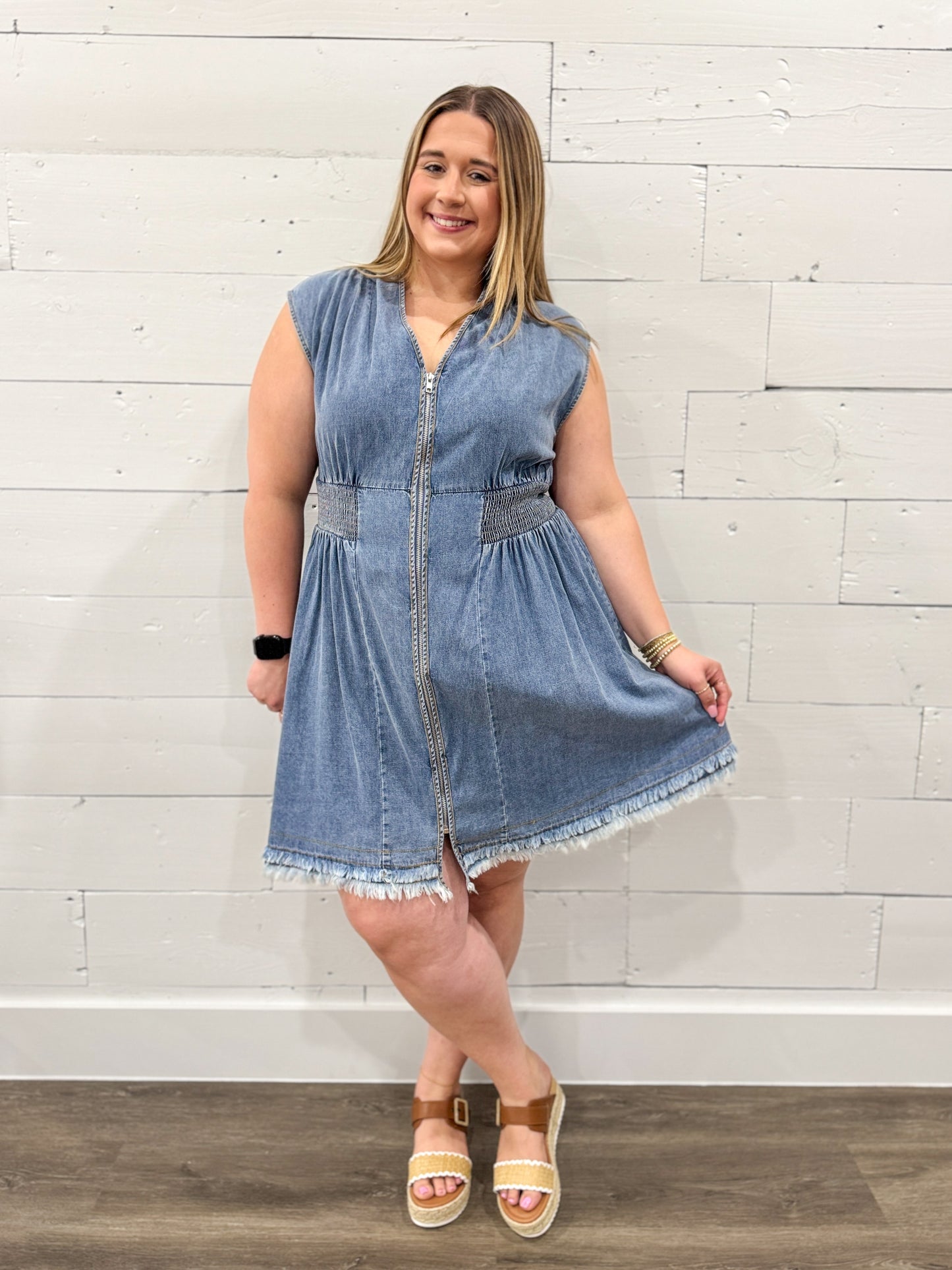 Woman wearing a denim dress against a white brick wall.