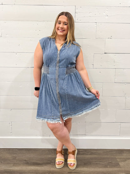 Woman wearing a denim dress against a white brick wall.