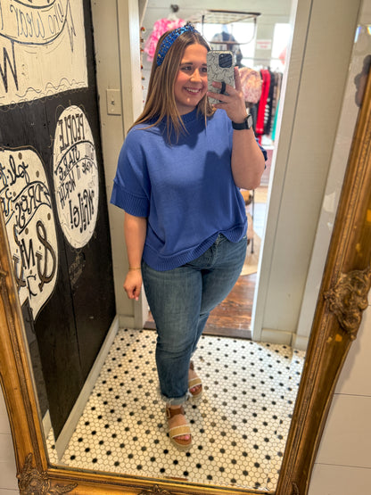 Woman taking a mirror selfie wearing a blue sweater and jeans in a store.