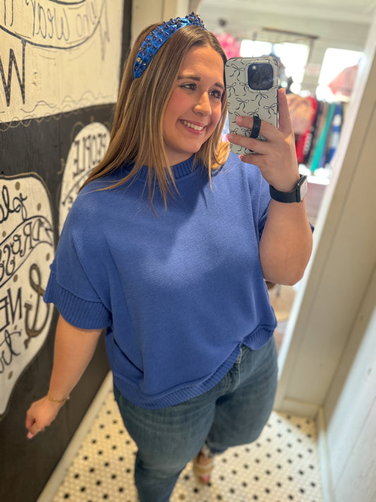 Woman taking a mirror selfie wearing a blue sweater and jeans indoors.
