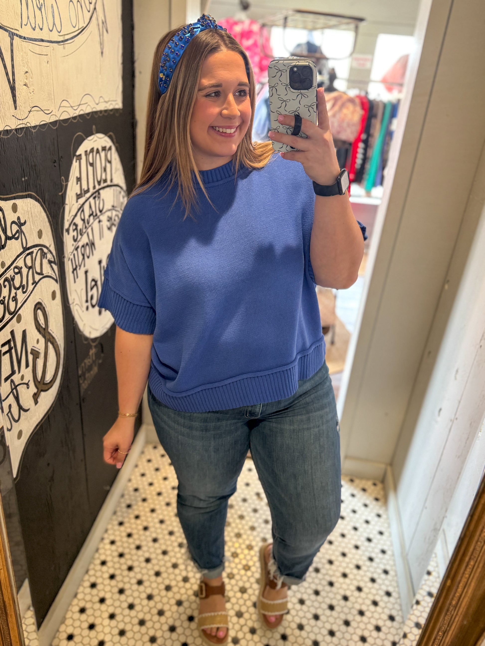 Woman taking a mirror selfie wearing a blue sweater and jeans in a store.