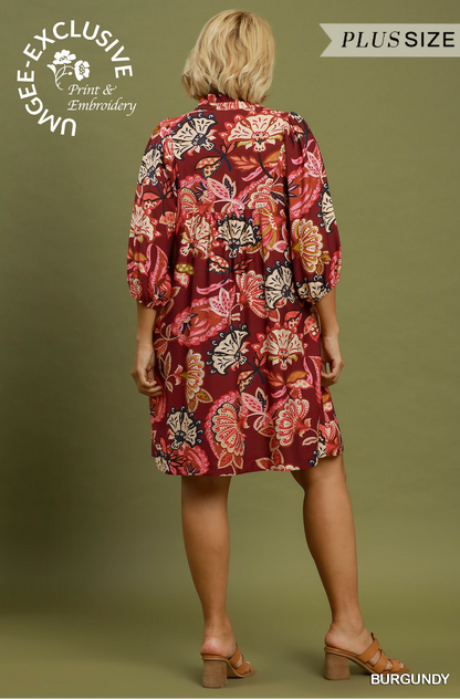 A woman shown from the back wearing a burgundy floral print shirt dress with three-quarter sleeves and a tie waist, standing against an olive green background. Text overlays include 'UNGEE-EXCLUSIVE Print & Embroidery', 'PLUSSIZE', and 'BURGUNDY'.