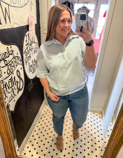 Woman taking a mirror selfie wearing a striped shirt and jeans in a room with decorative elements.