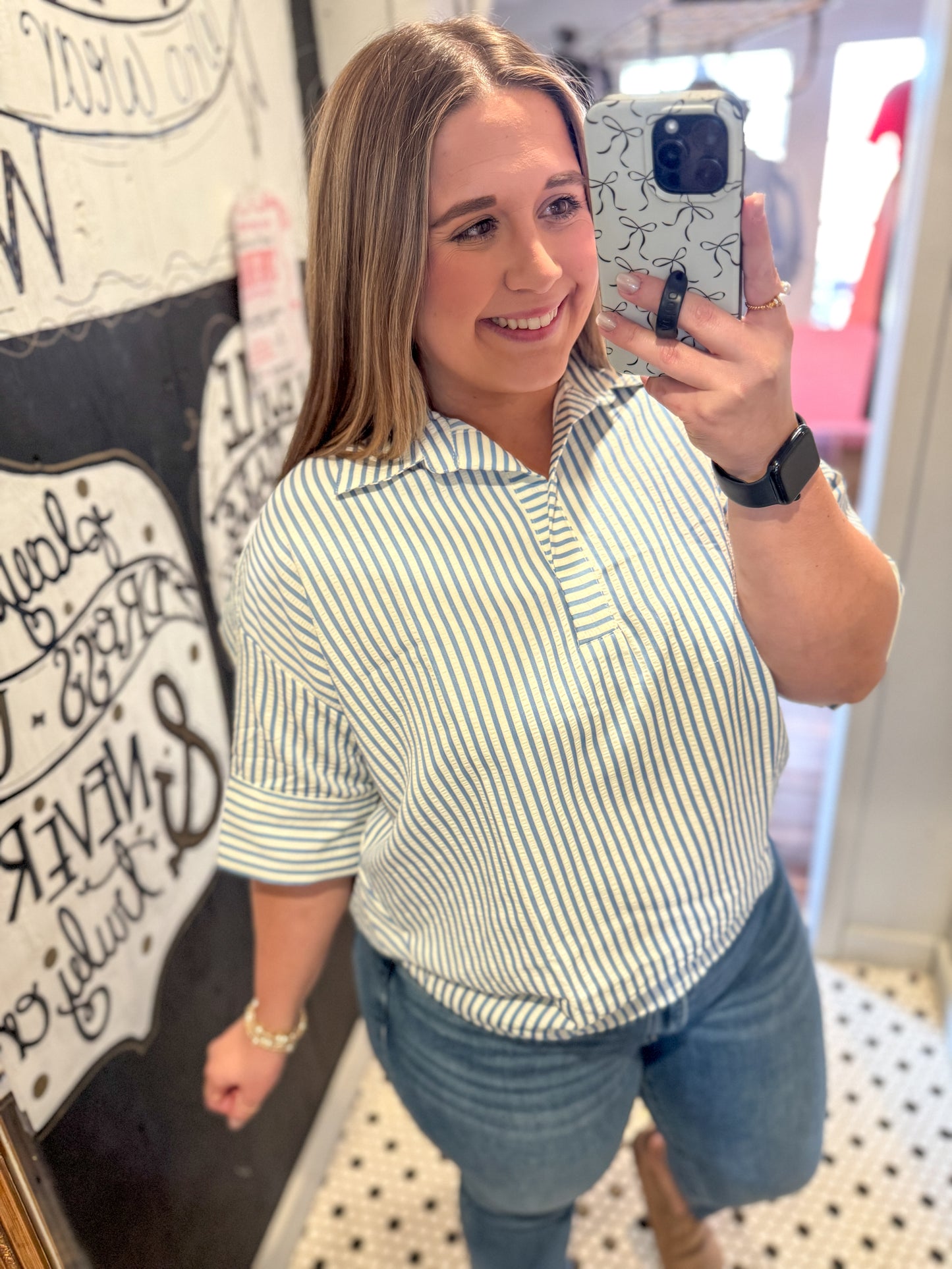 Woman taking a mirror selfie wearing a striped shirt and jeans in a store.