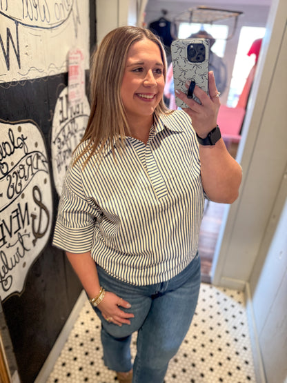 Woman taking a mirror selfie wearing a striped shirt and jeans in a room with decor.