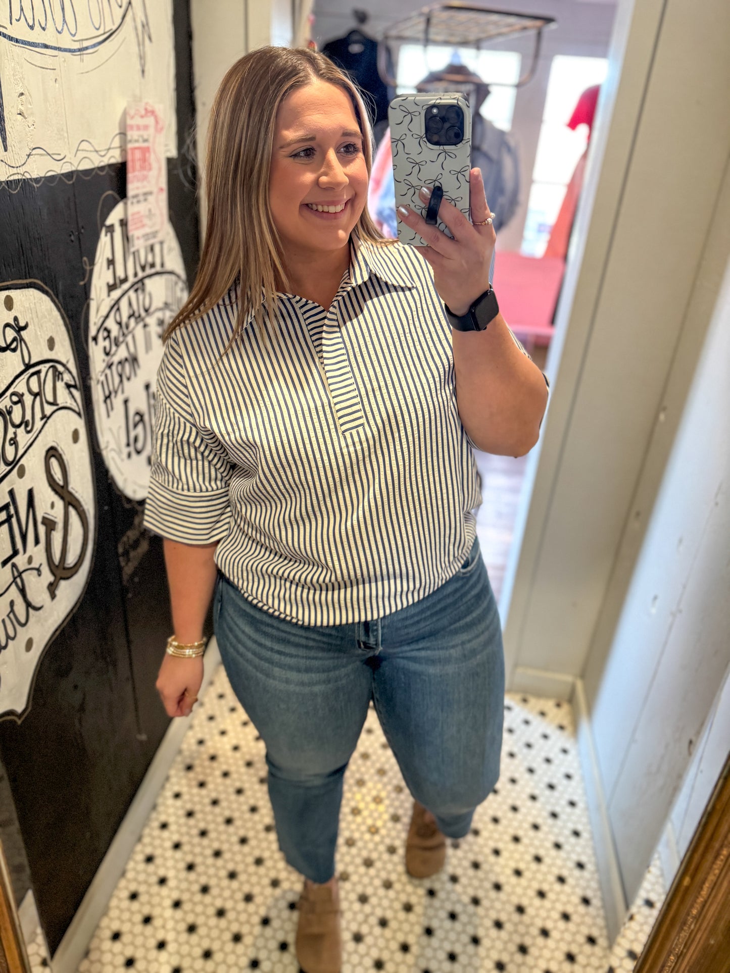 Woman taking a mirror selfie wearing a striped shirt and jeans in a store.