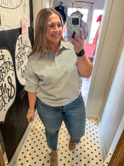 Woman taking a mirror selfie wearing a striped shirt and jeans in a store.