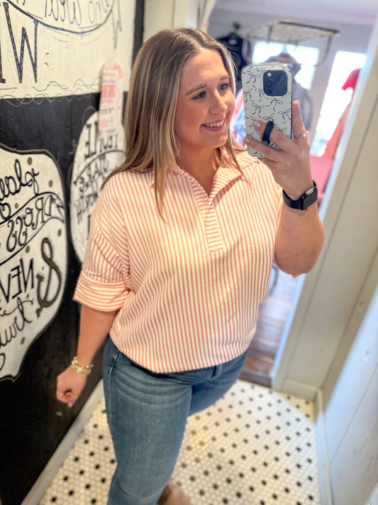 Woman taking a mirror selfie wearing a pink striped shirt and blue jeans in a store.