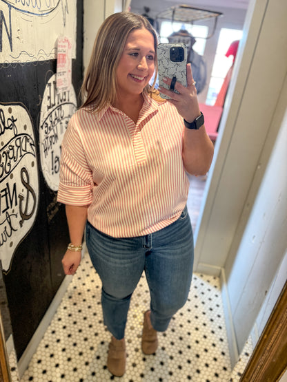 Woman taking a mirror selfie wearing a striped shirt and jeans indoors.