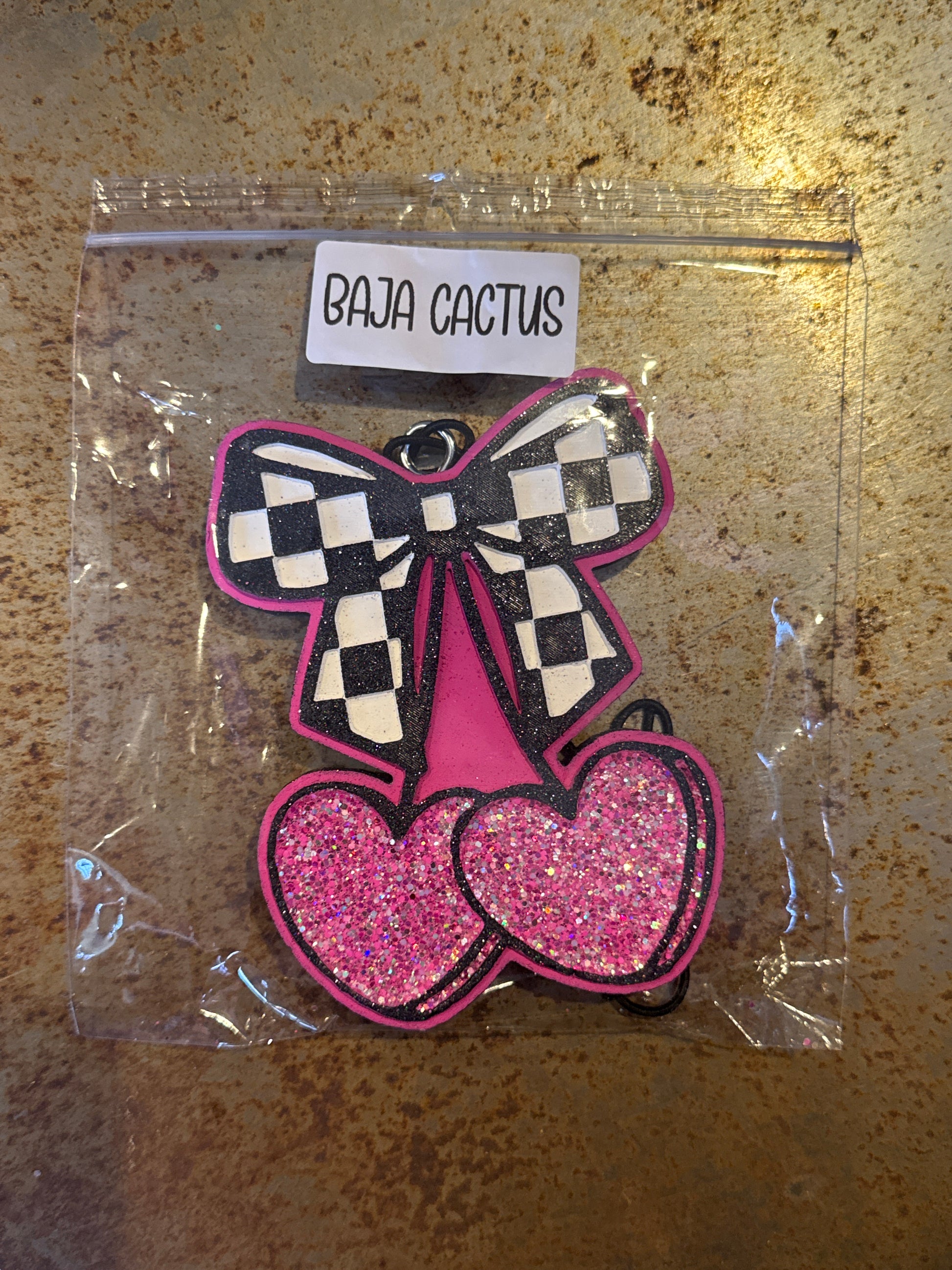 Pink and black checkered butterfly patch in clear packaging on a textured surface