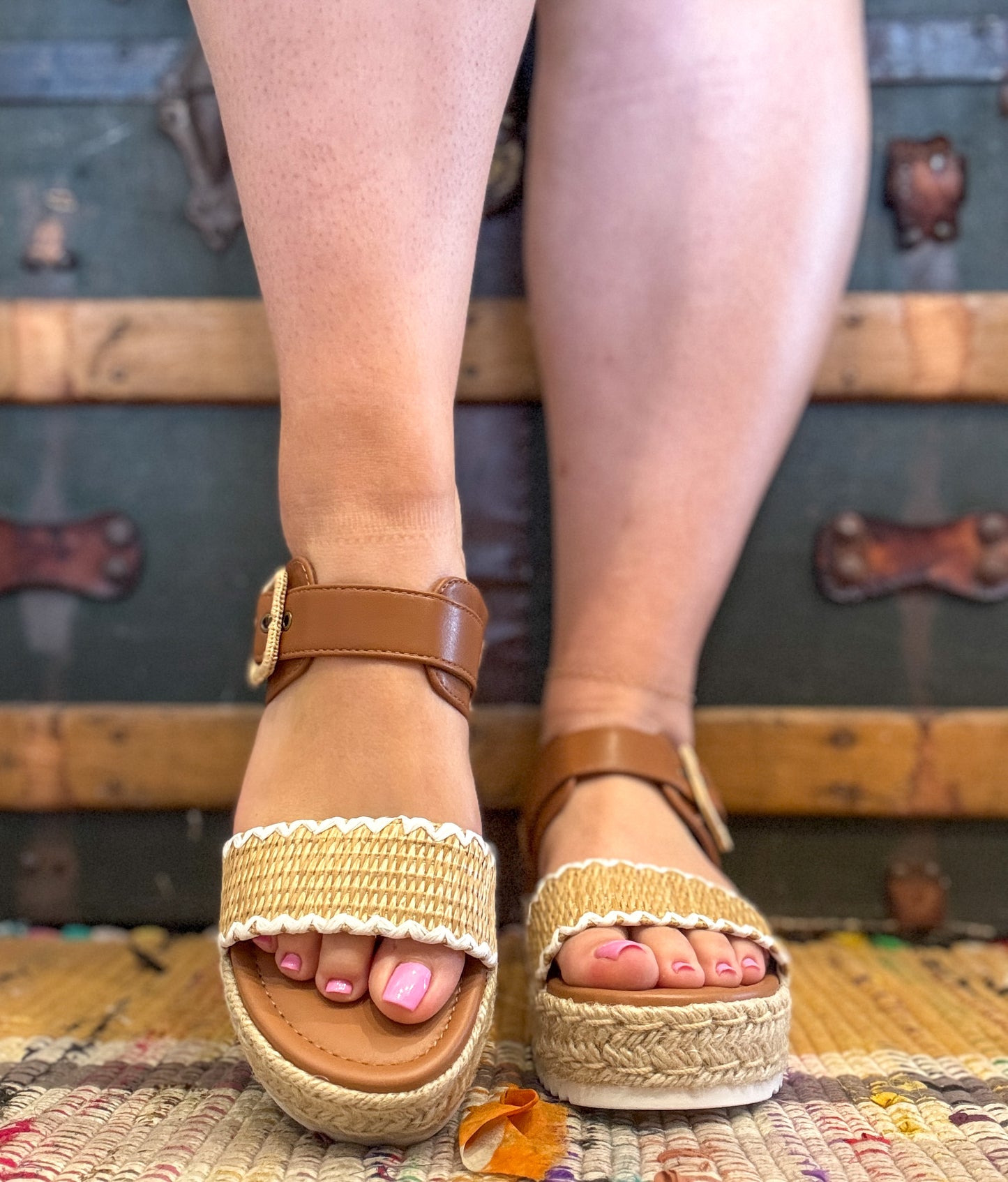 Brown sandals with beige straps worn by a person on a textured surface.